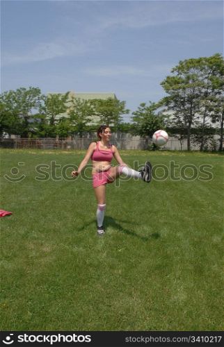 Soccer woman practice her skills alone on a big soccer field in thecity, in pink shorts and sports bra, in beautiful sunshine.