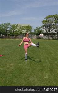 Soccer woman practice her skills alone on a big soccer field in thecity, in pink shorts and sports bra, in beautiful sunshine.