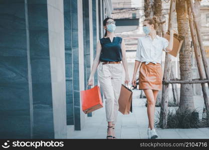 social distancing new normal concept.portrait of two happy girls walking together wearing medical face masks, walking outdoors in the evening near mall after covid epidemic , holding shopping bags.