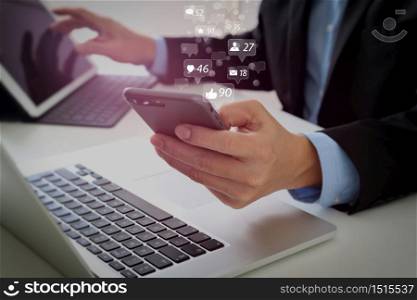 Social media and Marketing virtual icons screen concept.Hands of businessman using mobile phone in modern office with laptop and digital tablet computer