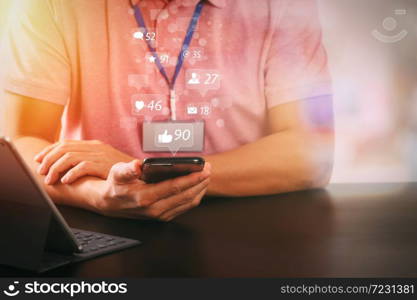 Social media and Marketing virtual icons screen concept.businessman in pink t-shirt working with smart phone and digitl tablet computer on wooden desk in modern office with glass reflected view