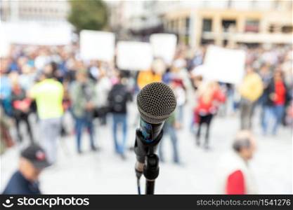 Social protest or public demonstration. Microphone in focus against unrecognizable crowd of people.