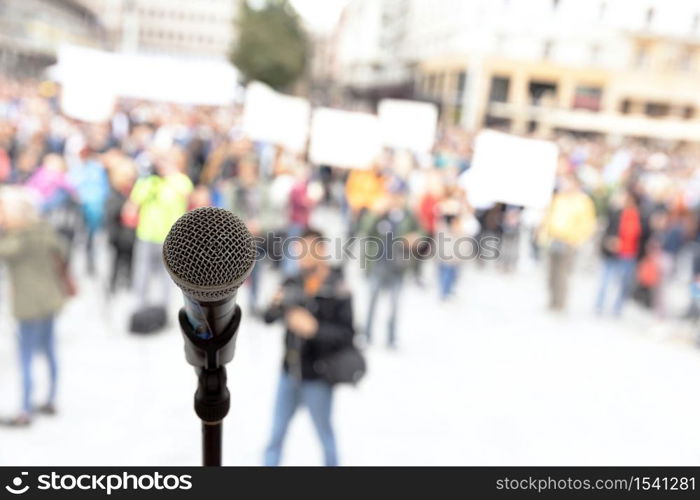 Social protest or public demonstration. Microphone in focus against unrecognizable crowd of people.