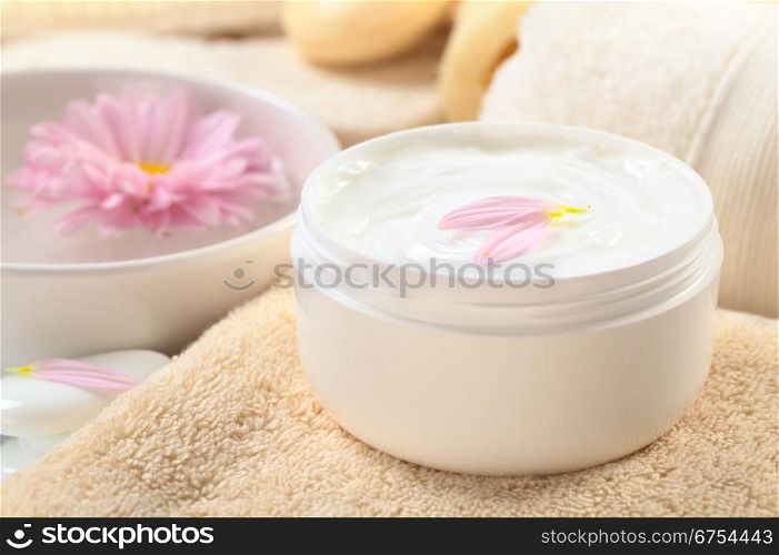 Soft body, hand and face cream with pink petals on top in a bathroom/spa setting (Selective Focus, Focus on the horizontal/back petal on the cream). Soft Body, Hand and Face Cream