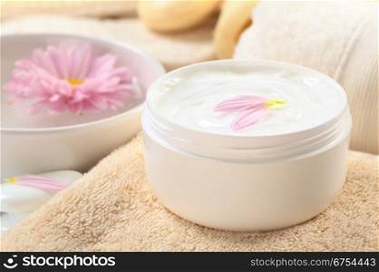 Soft body, hand and face cream with pink petals on top in a bathroom/spa setting (Selective Focus, Focus on the horizontal/back petal on the cream). Soft Body, Hand and Face Cream