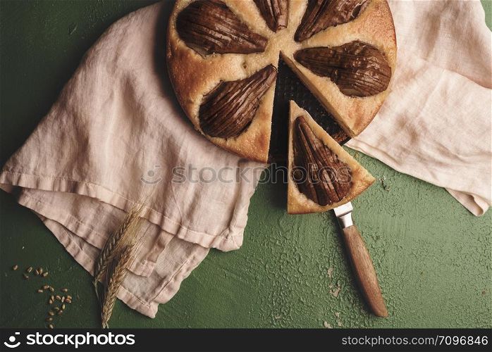 Soft cake with whole pears on a kitchen towel. Above view with a sliced fruit pie. Single slice of fruitcake