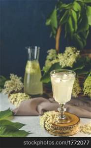 Soft drink with ice cubes from elderflower syrup, juice or champagne in a glass on a light gray table surface, selected focus, narrow depth of field