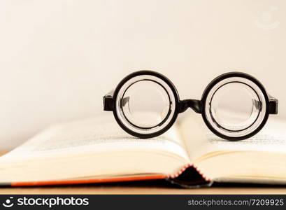 soft focus glasses with blur books stack on wooden desk in university or public library room or book store.concept of knowledge and education.