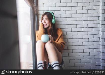 Soft Focus of Young Woman Relaxing with Music From Headphone in Cozy House Nearby Window, Enjoying with Morning Sunshine and Hot Coffee