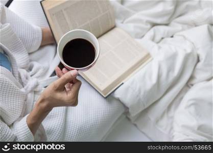 Soft photo of woman on the bed with old book and cup of coffee and copy space.