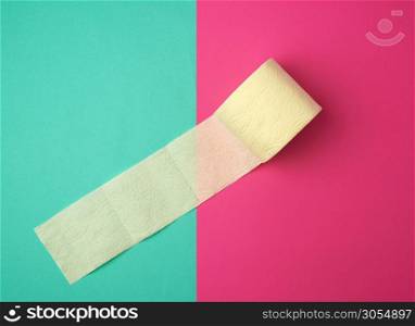soft yellow toilet paper in a roll on a green-pink background, top view