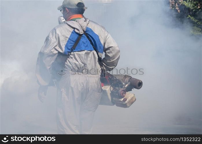 Softly focus of health personal worker using fogging machine spraying chemical to eliminate mosquitoes and prevent dengue fever in the midst of many chemical fumes at general location in community