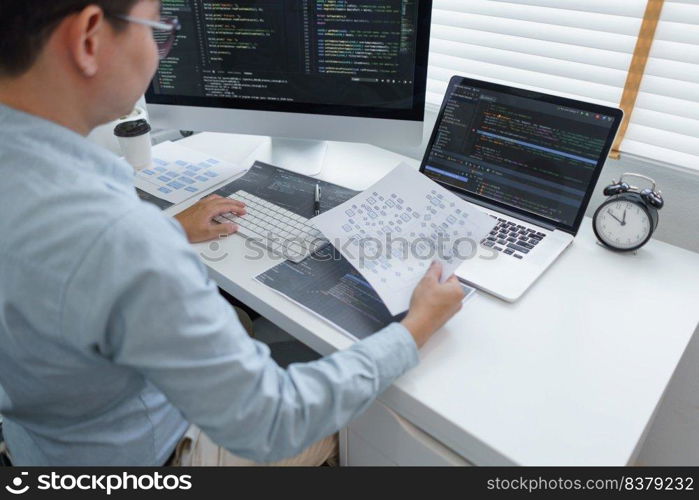 Software development concept, Male programmer read data on document while programming on computer.