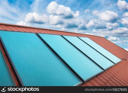 Solar cells on the red house roof over blue sky with clouds