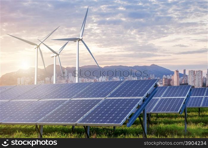 solar panels and wind turbines under sky and clouds with city on horizon. Sunrise. Solar panels and wind turbines with city