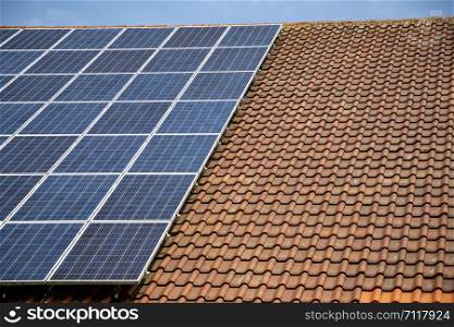 solar panels on roof of house. horizontal orientation, blue sky, gray panels on brown roof.