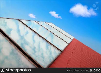 Solar panels on the red house roof with blue sky and clouds