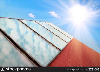 Solar panels on the red house roof with blue sky, sun and clouds