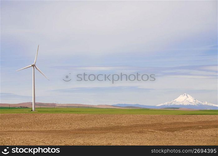 Solar powered wind turbine in remote field with snow covered mountain in background