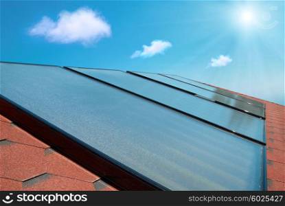 Solar water heating cells on the red house roof under shining sun and clouds.