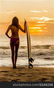 Solarised style photograph rear view of beautiful sexy young woman surfer girl in bikini with white surfboard on a beach at sunset or sunrise