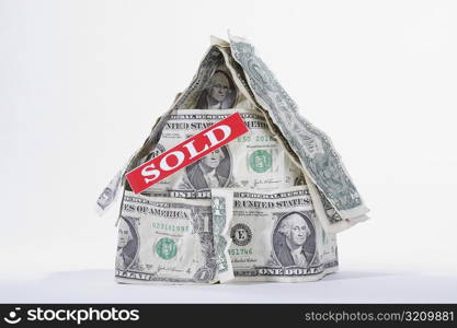 SOLD signboard on a miniature house made up of US dollar bills