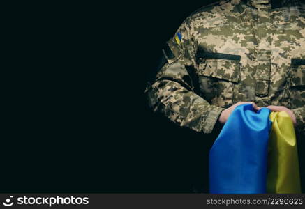 soldier of the Ukrainian armed forces stands with a blue-yellow flag of Ukraine on a black background. Honoring veterans and commemorating those killed in the war. Copy space