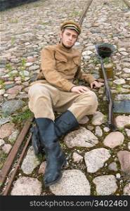 Soldier with gun and boiler in uniform of World War I, resting on the pavement. Costume accord the times of World War I. Photo made at cinema city Cinevilla in Latvia.