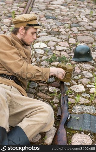 Soldier with gun and boiler in uniform of World War I, resting on the pavement. Costume accord the times of World War I. Photo made at cinema city Cinevilla in Latvia.