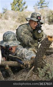 Soldiers aiming machine gun, leaning on log