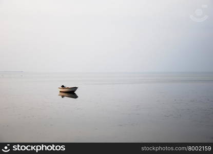 Solitude small rowing boat in the water by a gray and misty coast