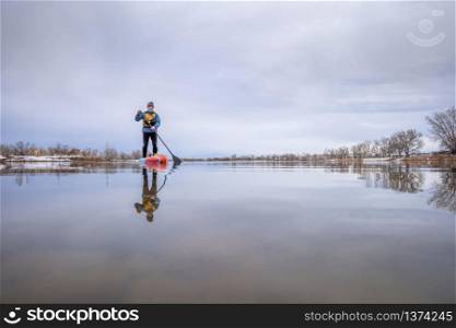 solo lake paddling as social distancing recreation during coronavirus pandemic, a senior male paddler on stand up paddleboard in early spring in Colorado