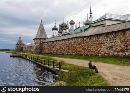 Solovki, Russia, July, 19, 2015. Spaso-Preobrazhensky Solovetsky monastery in summer, cloudy sky. View from the Holy Lake. Women artist is drawing monastery wall.