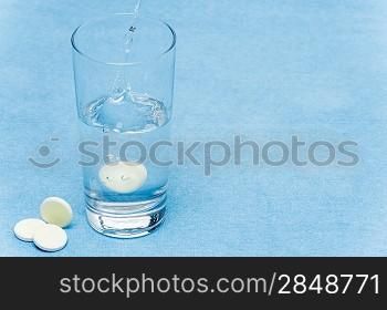 Soluble tablet throw in water glass on blue background
