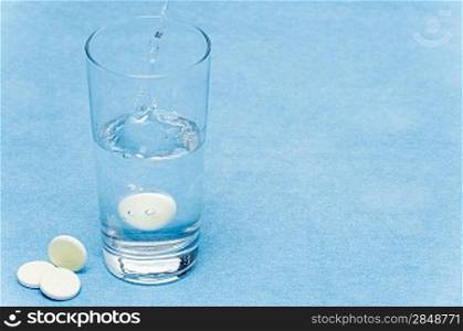 Soluble tablet throw in water glass on blue background