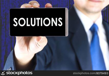 SOLUTIONS word on mobile phone screen in blurred young businessman hand and digital technology background, business concept