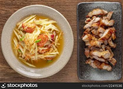Som Tum Thai, Som Tam Thai, Thai food, spicy papaya salad and fried pork in ceramic plate on rustic natural wood texture background, top view