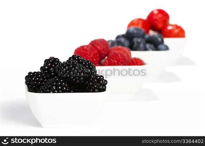 some bowles filled with wild berries. some bowls filled with wild berries on white background blackberries in front