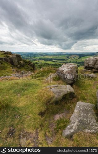 Some rocks on the edge of a hill at Baslow Edge with the countryside view beyond, in the Peak district, Derbyshire