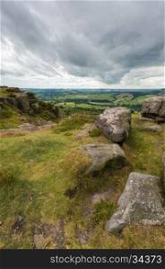 Some rocks on the edge of a hill at Baslow Edge with the countryside view beyond, in the Peak district, Derbyshire