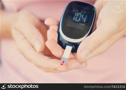 Someone measuring blood sugar level with blood glucose metr, world diabetes day concept, toned. Measurnig blood sugar level