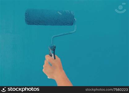Someone painting white wall in blue color hand holding paint roller. Someone painting wall