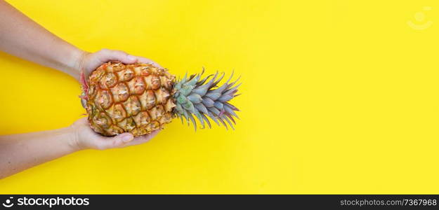 someones hands holding raw pineapple on yellow background banner. pineapple fruit, minimal style