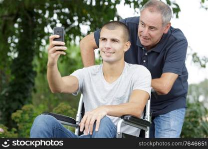 son and father in wheelchair at park taking selfie