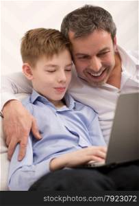 Son and father with laptop at home. They found something interesting and looking at screen. Happy dad and son with laptop at home