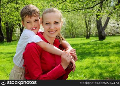 son embraces behind mother in park in spring