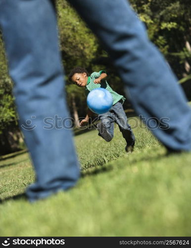 Son running and kicking ball towards father in park.