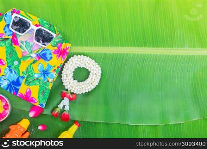 Songkran Festival background with jasmine garland Flowers in a bowl of water, perfume and limestone on a green wet banana leaf background.