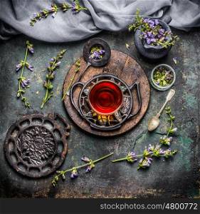 Soothing cup of herbal tea with freshest organic ingredients: herbs and flowers on rustic vintage background with tea tools, top view