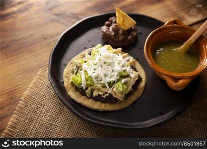 Sopes de Pollo. Traditional homemade Mexican appetizer prepared with fried corn dough covered with refried beans, green or red sauce, lettuce, cheese, onion and shredded chicken